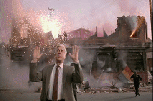 Leslie Nielsen waves his hands and shouts 'Nothing to see here' standing in front of a partly demolished building with explosions going off, people running away. Clip from 'The Naked Gun'